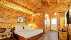 A wooden cabin bedroom with a bed, a nightstand, a dresser, and a painting on the wall. - FabHotel The Village Boutique Resort - Nr Chapora Fort, Vagator (Vagator)