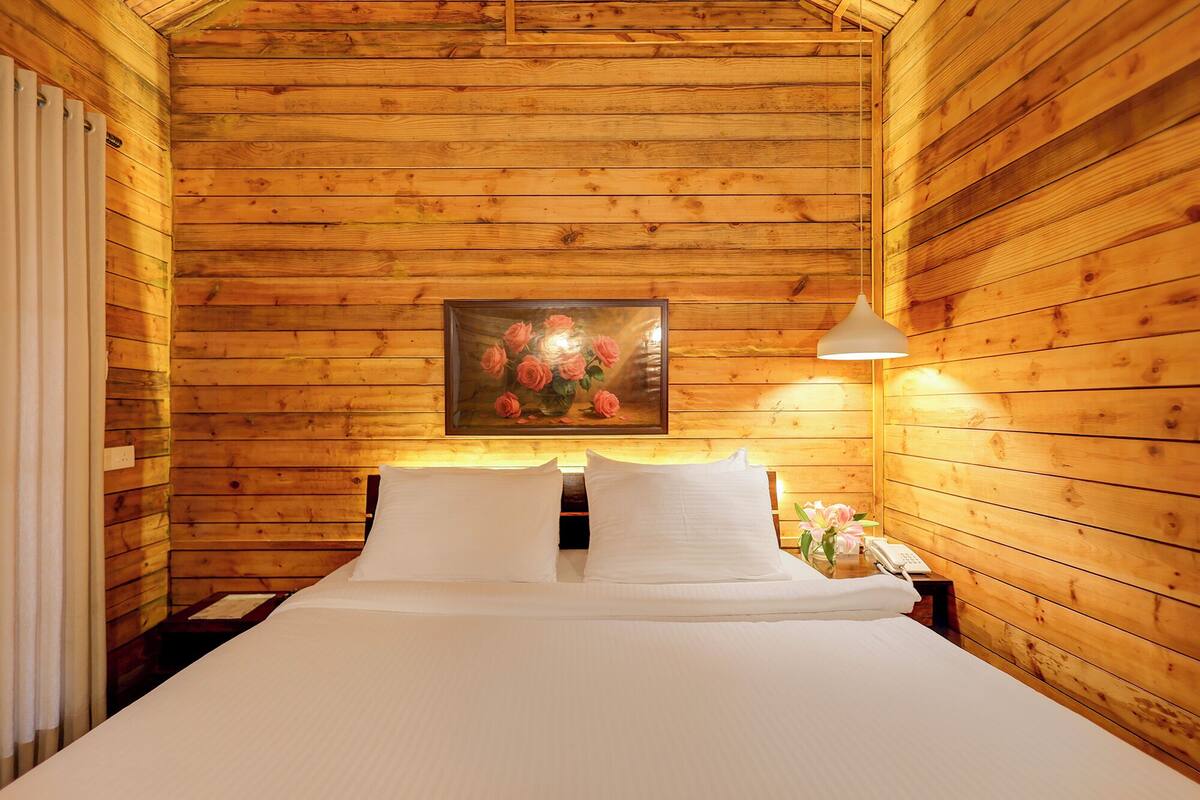 Een knus houten vertrek met een bed, een nachtkastje, een lijst met rozen en een bedlamp.