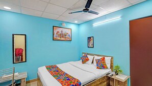 Un dormitori amb un llit, una taula de treball, una cadira, un ventilador de sostre i obra d'art a les parets.