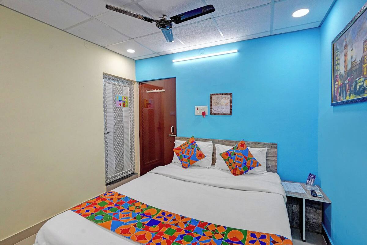 A bedroom with a bed, a ceiling fan, a nightstand, a wall clock, and a door.