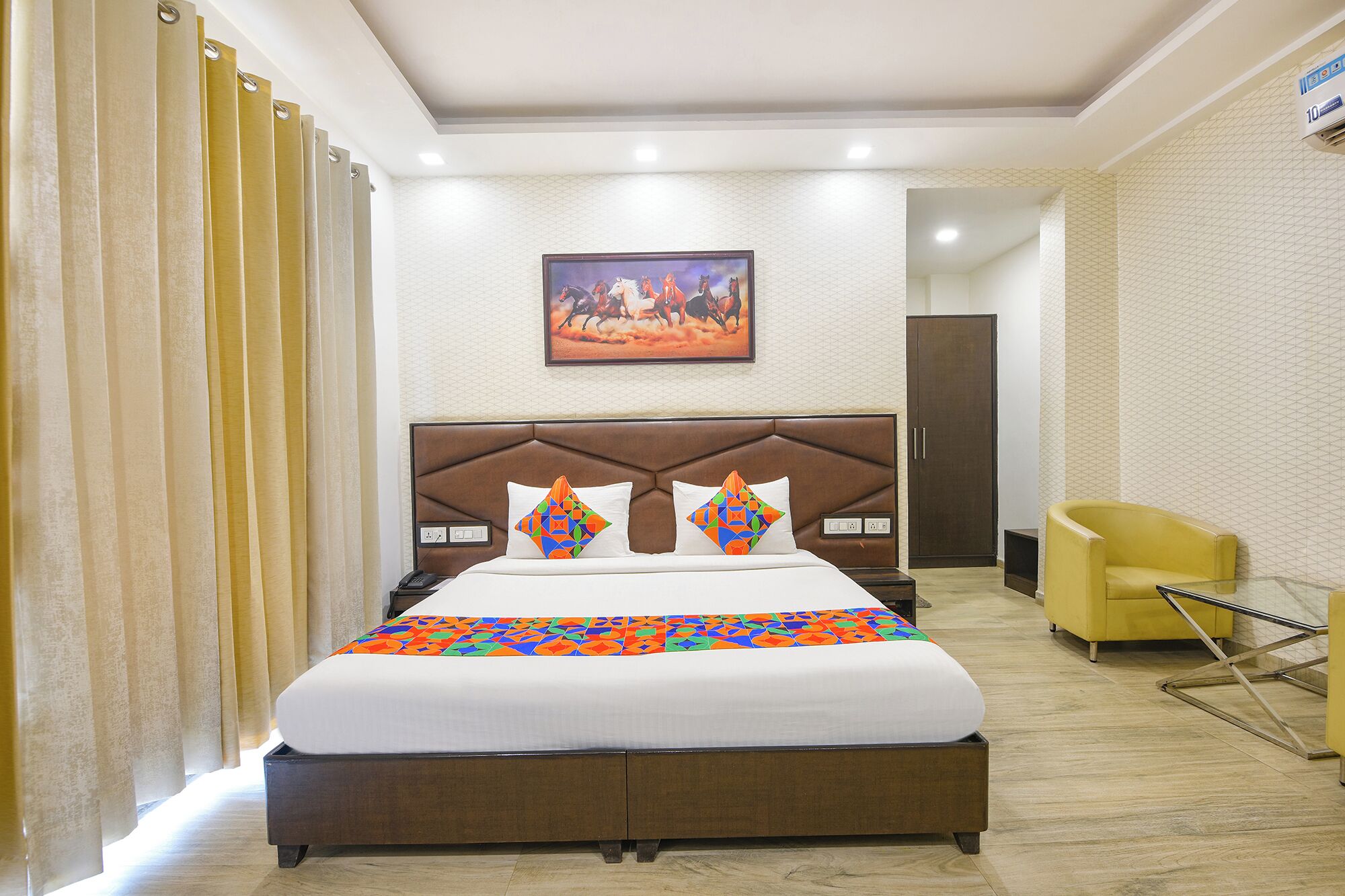 A hotel room with a large bed, a headboard, a painting on the wall, and a yellow armchair.