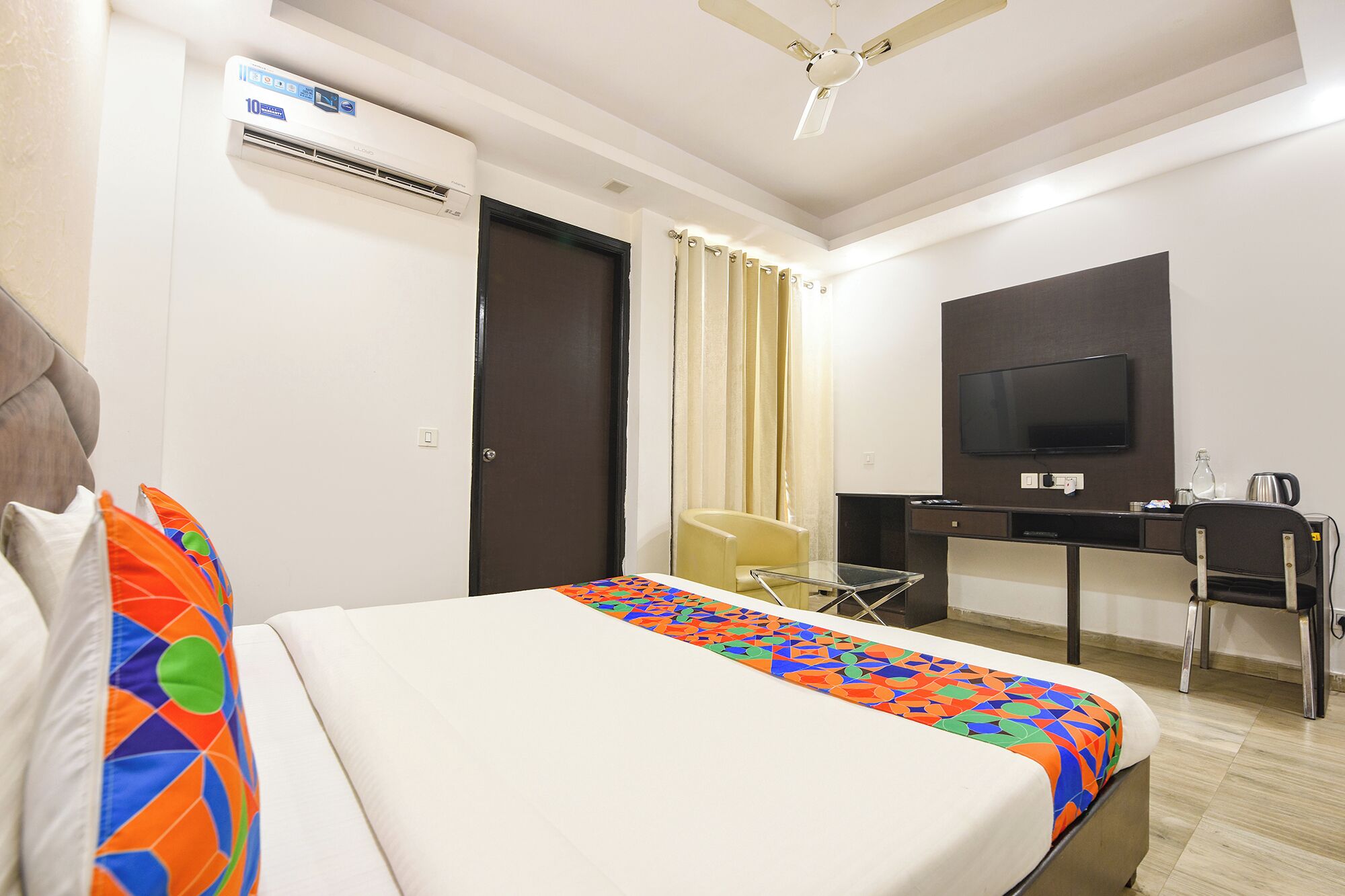 A hotel room with a bed, a desk, a television, and an air conditioning unit.