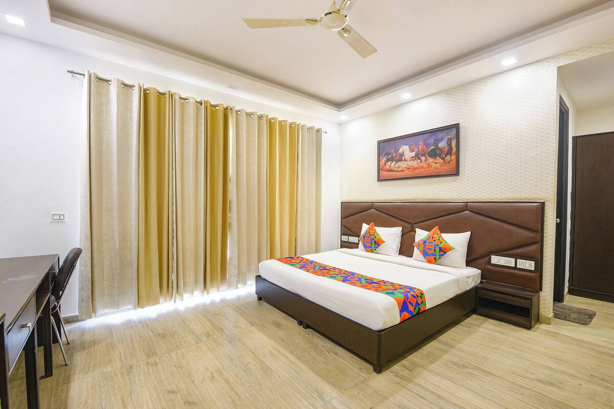 Une chambre d’hôtel avec un lit, un bureau, une chaise, un ventilateur de plafond et un tableau au mur.