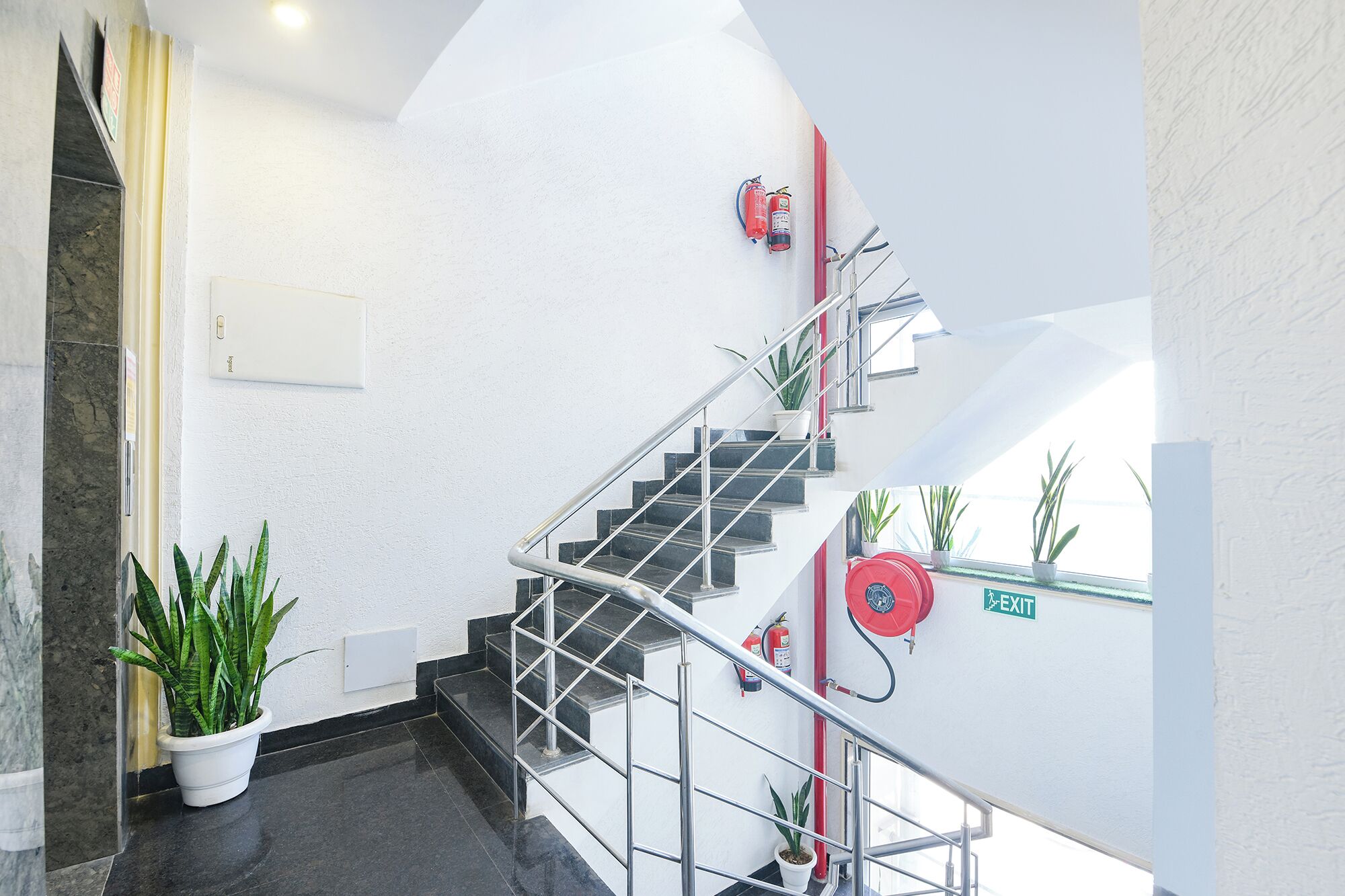 A staircase with metal railings, potted plants, and fire extinguishers on the walls.