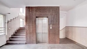 A modern interior with a central elevator, a staircase on the left, and a plain wall on the right. - Fabhotel Pantao Stay (Noida)