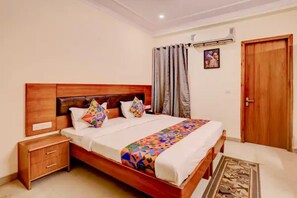 A neatly arranged bedroom with a wooden bed, a nightstand, a wooden door, and a wall-mounted air conditioner. - Fabhotel Pantao Stay (Noida)