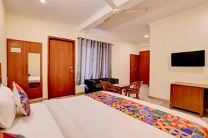 A hotel room with a bed, a desk, a chair, a television, and a ceiling fan. - Fabhotel Pantao Stay (Noida)
