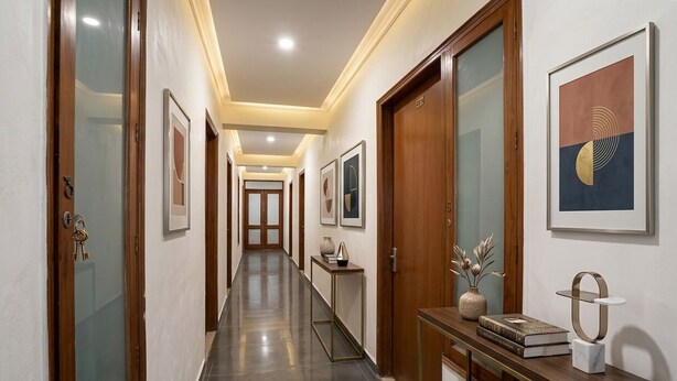 A hotel hallway with wooden doors, framed artwork, a console table with books and decorative items, and a tiled floor. - Fabhotel Pantao Stay (Noida)