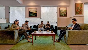 A group of people seated on sofas in a modern lounge area with a green rug, a wooden coffee table, and artwork on the walls. - Fabhotel Pantao Stay (Noida)