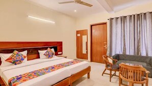 A hotel room with a bed, a wooden headboard, a sofa, and a chair. - Fabhotel Pantao Stay (Noida)