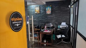 Despatx modern amb una paret de pedra fosca, un escriptori amb un ordinador i una cadira. Hi ha un cartell a la paret que diu "elysees SERVICED SUITES".