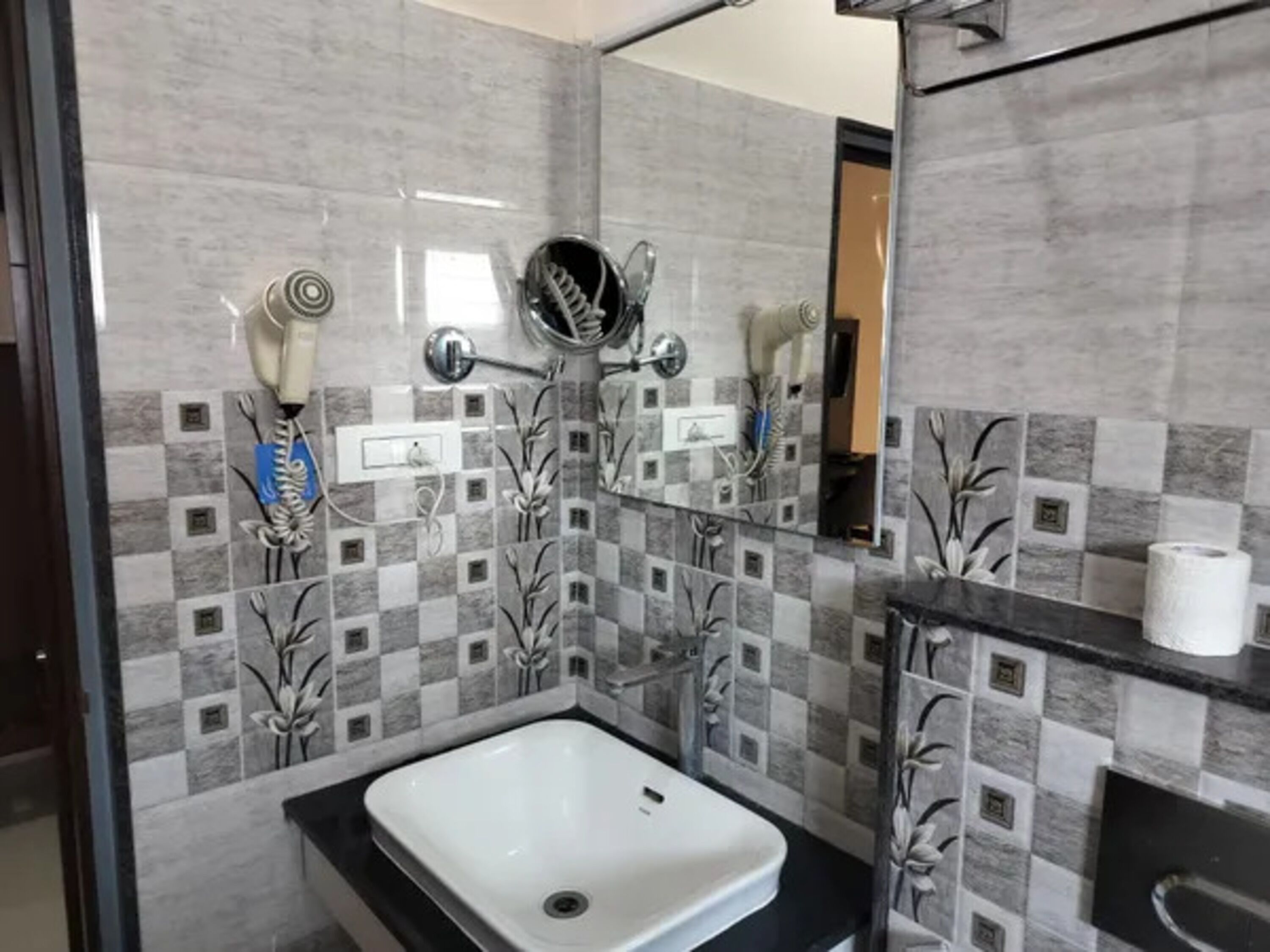 A bathroom with a white sink, a mirror, and a shower with a hairdryer and towel rack.