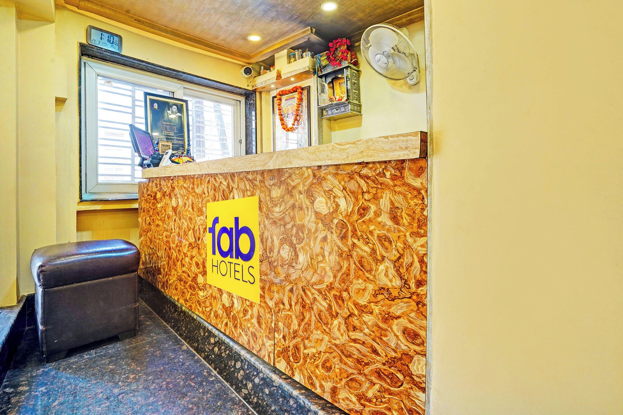 A reception desk with a marble-like design, a clock, and a window with blinds.