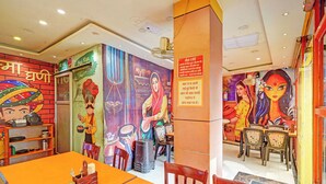Un ristorante con vivaci murales, un lungo tavolo arancione e decorazioni tradizionali indiane.