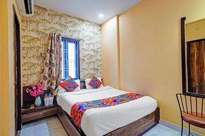 A bedroom with a bed, a window with blue shutters, a wooden chair, and a wall with a tree pattern. - Via Bharat (Varanasi)