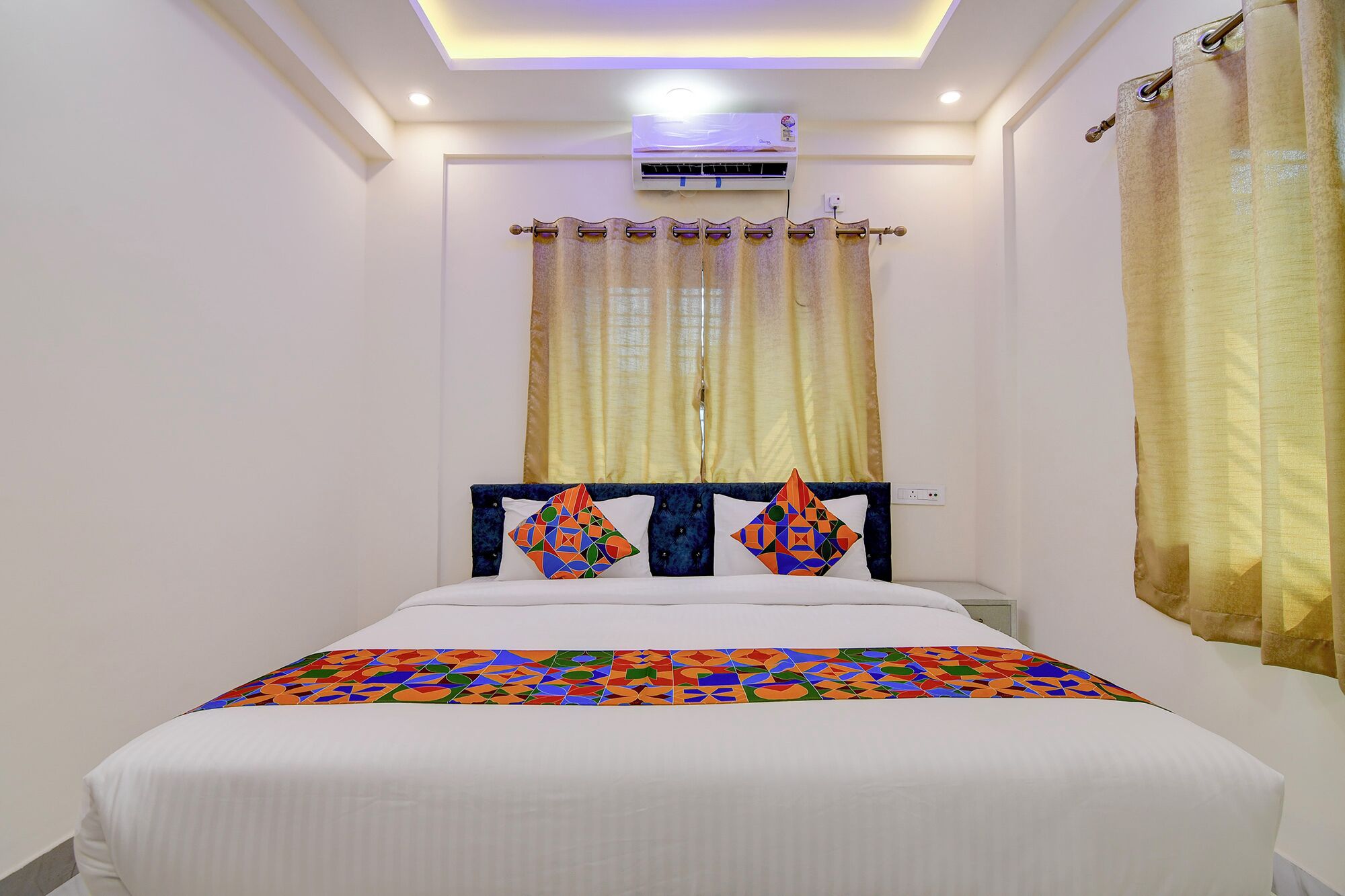 A bedroom with a bed, curtains, an air conditioning unit, and a ceiling light.