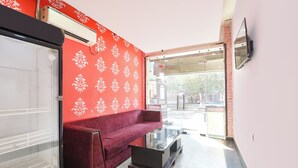 Ein Empfangsbereich mit roter Wand mit Muster, einem roten Sofa, einem Glastisch und einem an der Wand befestigten Fernseher.