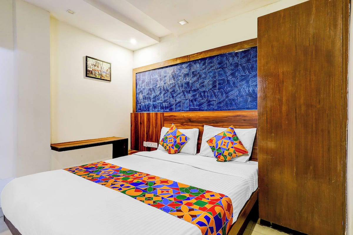 Een hotelkamer met een bed, een houten hoofdbord, een kleurrijk sprei en een schilderij aan de muur.