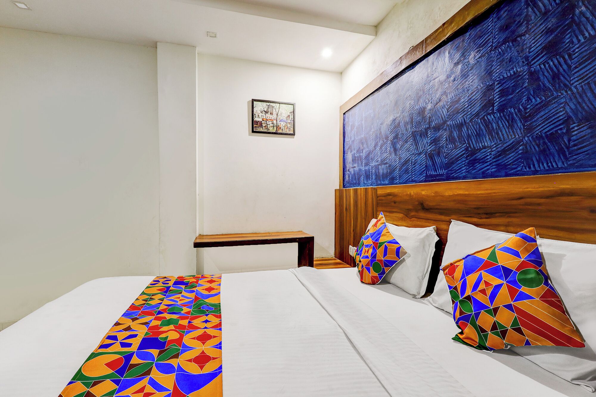 A hotel room with a large bed, a wooden headboard, a nightstand, and a painting on the wall.