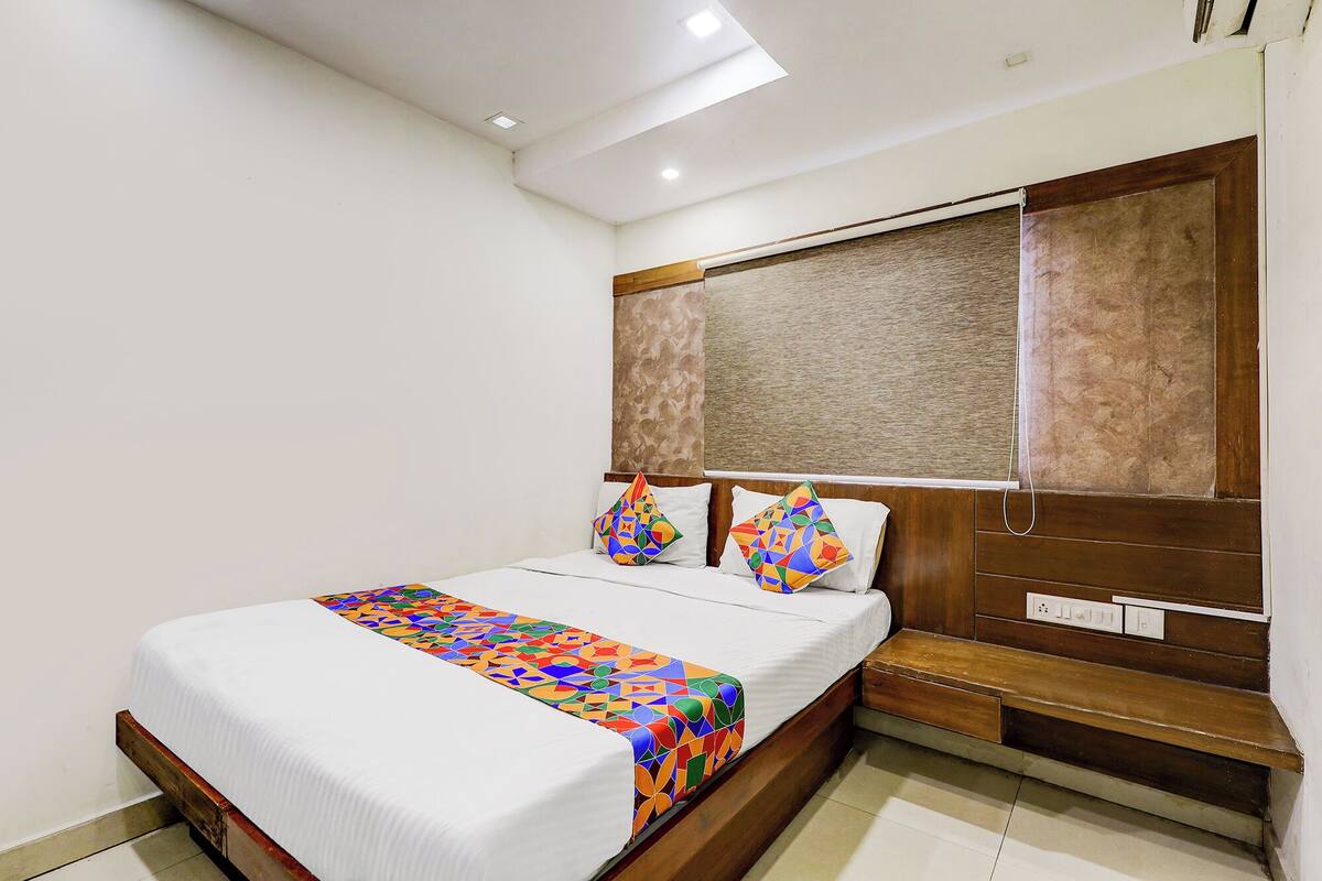 Een hotelkamer met een bed, een houten hoofdbord, een raam met zonwering en een nachtkastje.