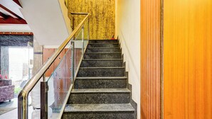 A staircase with a glass railing, leading to a room with a yellow wall and a wooden door. - Fabhotel Olive Grand (Chennai)