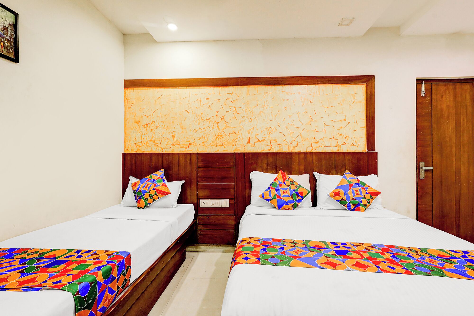 Een hotelkamer met twee enkele bedden, een houten hoofdbord, een groot abstract schilderij en een deur.