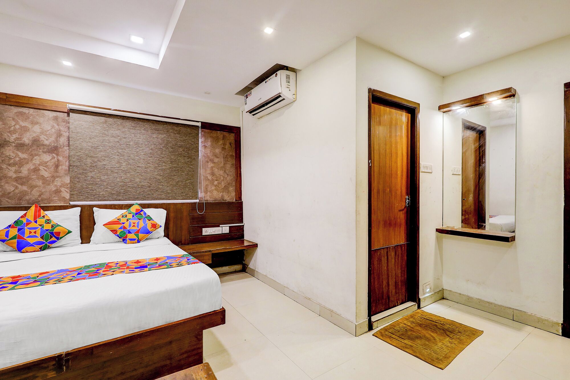 A bedroom with a bed, a bedside table, a wardrobe, a mirror, and an air conditioning unit.