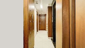 A hallway with wooden doors, a tiled floor, and a plain ceiling. - Fabhotel Olive Grand (Chennai)