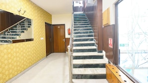 A hotel lobby with a marble staircase, a fire exit sign, and a wooden bench. - Fabhotel Guru Kripa Residency (Gurugram)