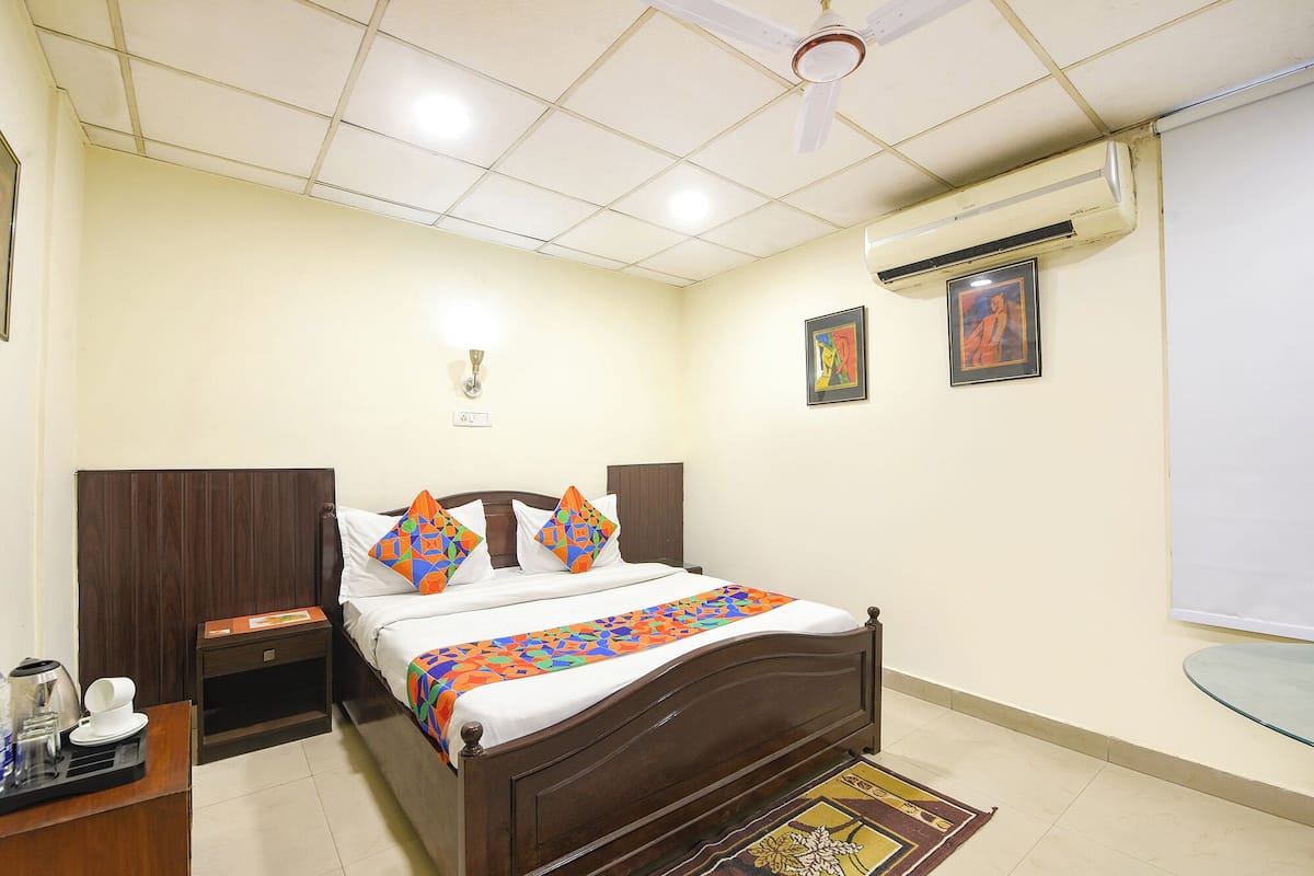 A hotel room with a bed, bedside tables, an air conditioning unit, a ceiling fan, and artwork on the walls.