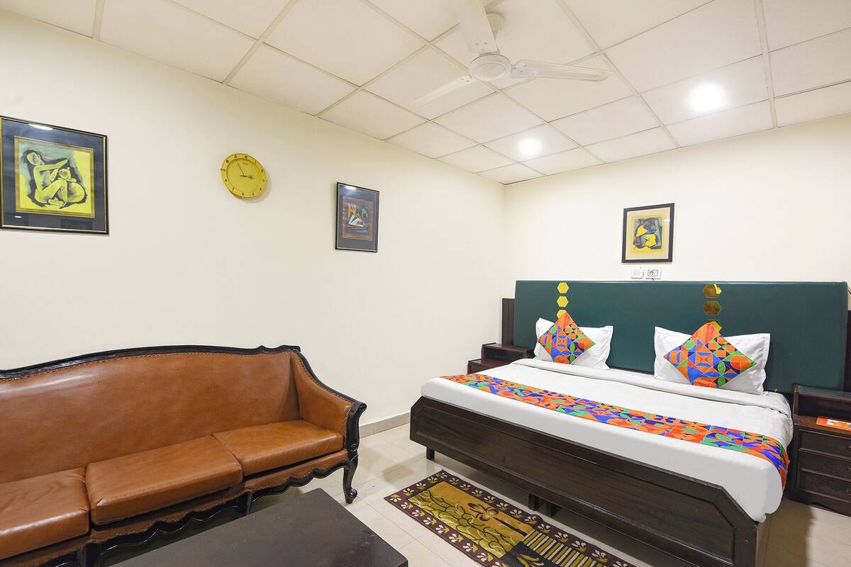 A bedroom with a bed, a brown leather sofa, a wooden nightstand, a wall clock, and framed artwork.