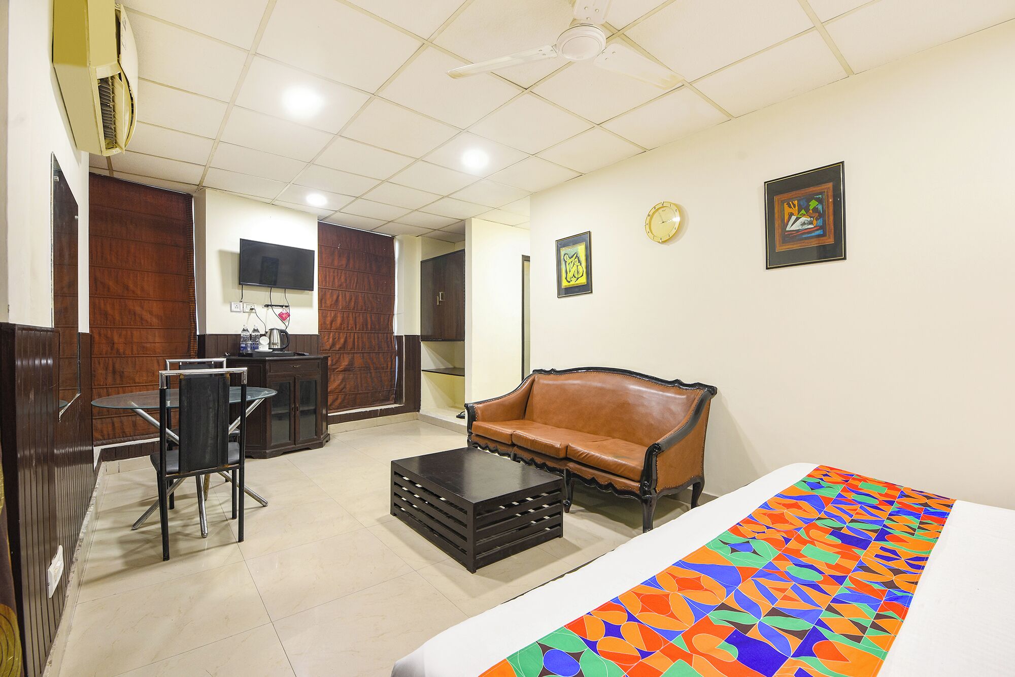 A hotel room with a bed, a sofa, a small table, a TV, and a kitchenette area.