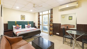 A hotel room with a bed, a desk, a chair, a couch, and an air conditioning unit. - Fabhotel Guru Kripa Residency (Gurugram)