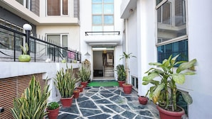 A narrow corridor with potted plants, a tiled floor, and a doorway leading to an interior space. - Fabhotel Guru Kripa Residency (Gurugram)