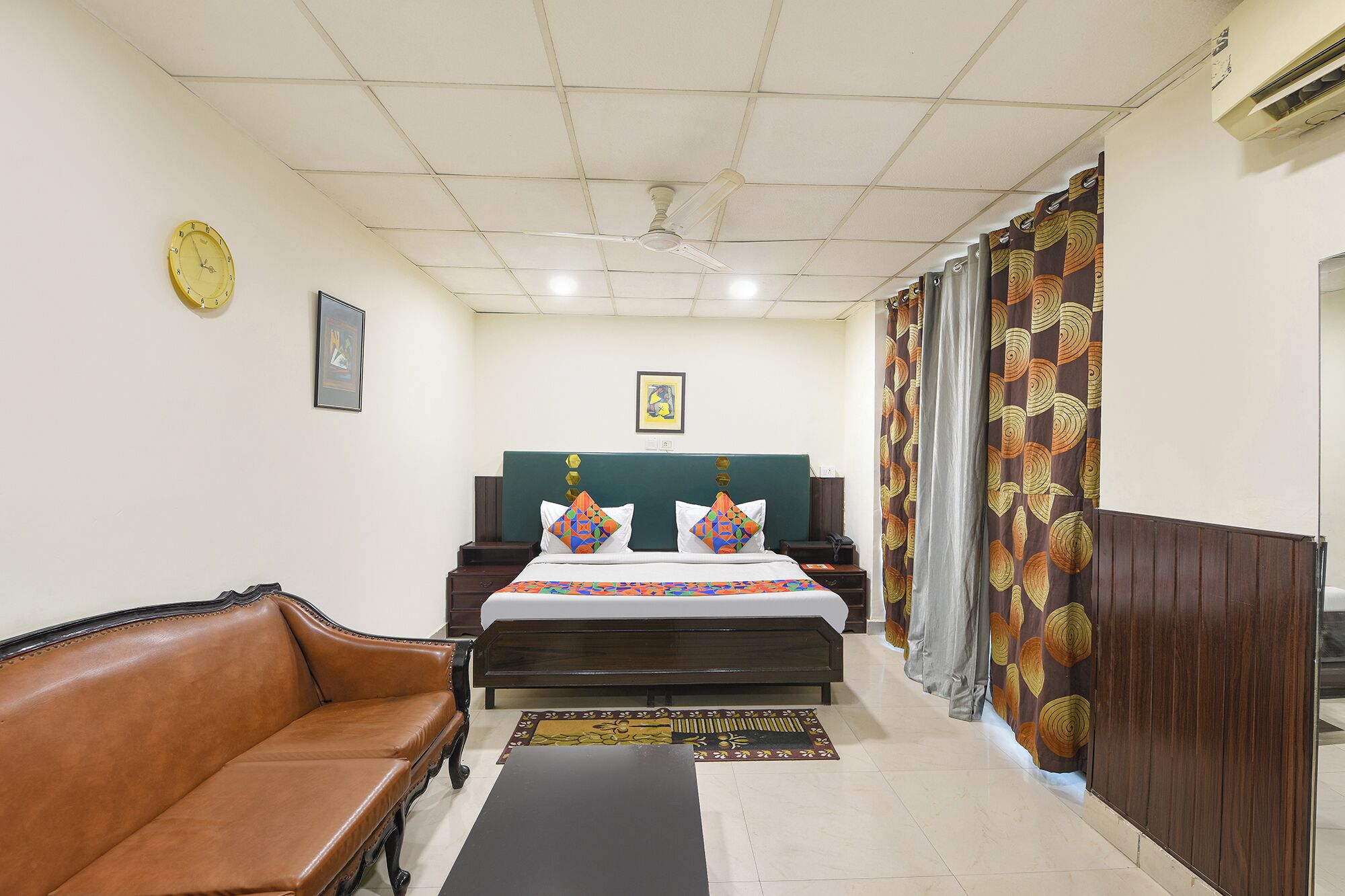 A hotel room with a bed, a sofa, a desk, a clock, and a ceiling fan.