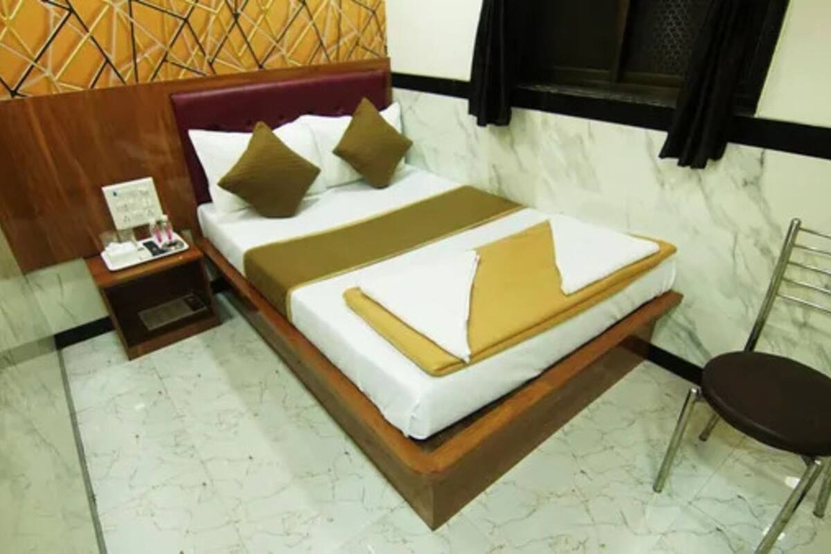 A hotel room with a bed, a nightstand, a chair, and a window with curtains.