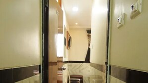 A hallway with a marble floor and walls, leading to a room with a table and chairs. - Fabhotel Star Hill (Mumbai)
