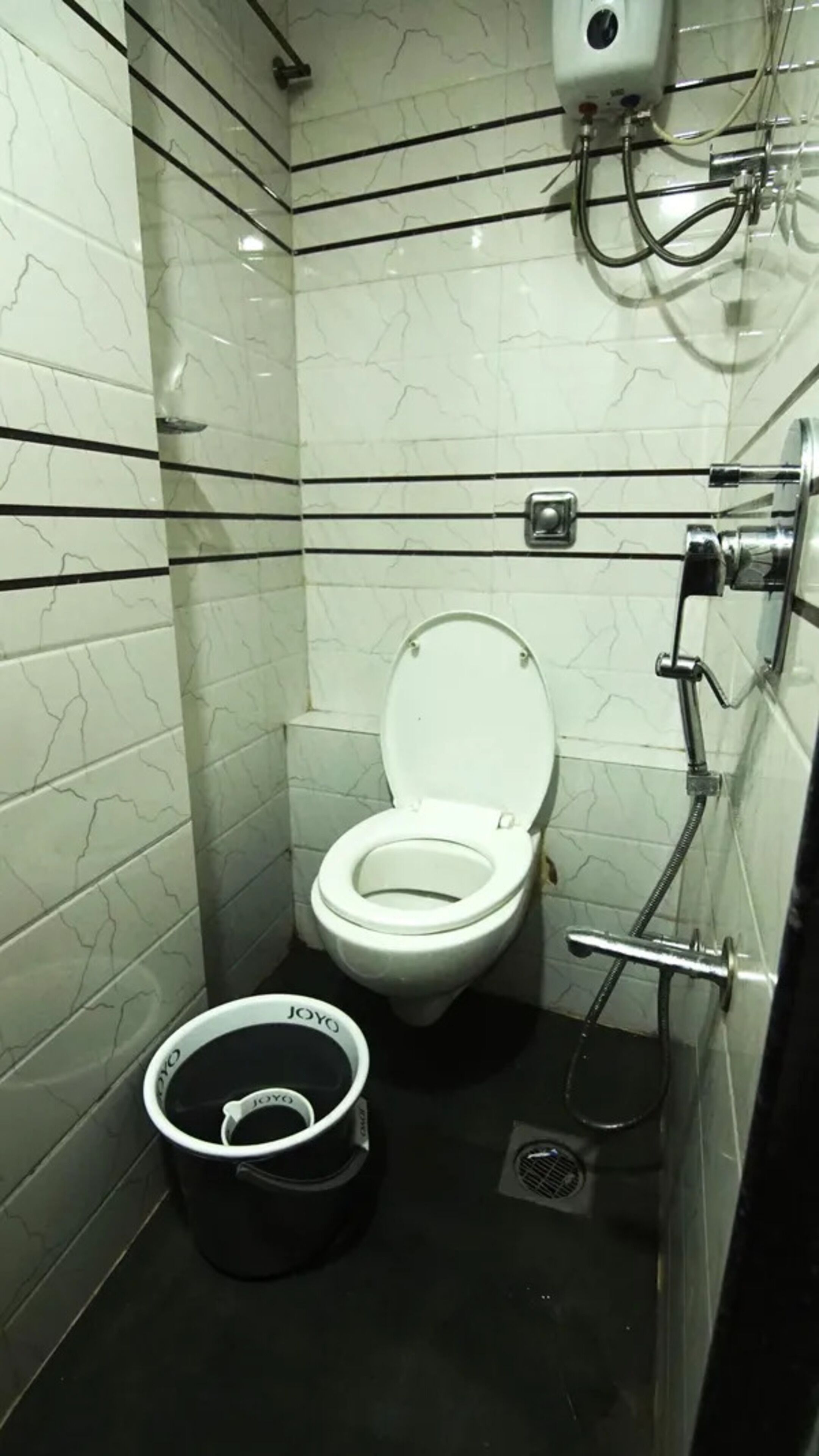 Un baño pequeño y moderno con inodoro, bidé y un cubo negro etiquetado 'JOYYO'.