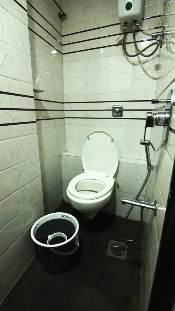 Une petite salle de bain moderne, équipée de toilettes, d’un bidet et d’un seau noir portant l’inscription « JOYYO ».