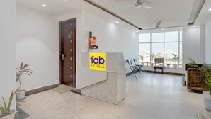A modern hotel lobby with a reception desk, seating area, and large windows offering city views. - Fabhotel Cozy Stay (Noida)