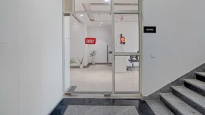 A modern interior with a glass door entrance, a sign indicating the 3rd floor, and a small office area with a desk and chair. - Fabhotel Cozy Stay (Noida)