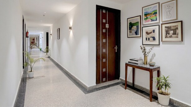 A hallway with a wooden door marked '319', a console table with books and a vase, and framed artwork on the wall. - Fabhotel Cozy Stay (Noida)