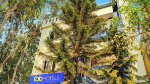 Um edifício com a placa 'fab hotels' e uma grande árvore em frente.