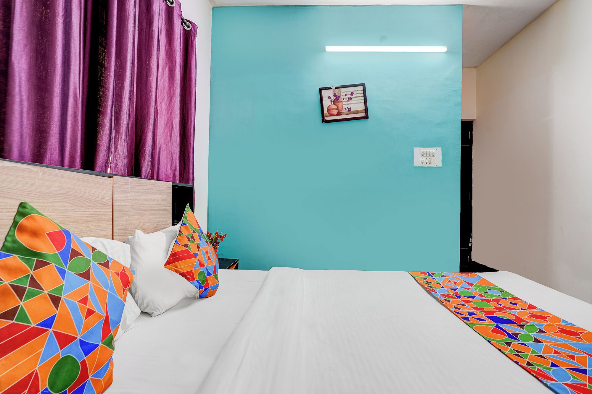 A bed with colorful pillows, a teal wall, and a framed picture.