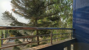 Uma varanda com grades de metal que dá para um jardim com várias árvores e um edifício ao fundo.