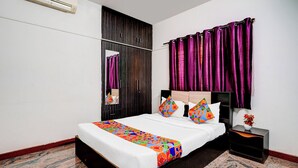 Quarto com cama, mesa de cabeceira, espelho e cortinas roxas.