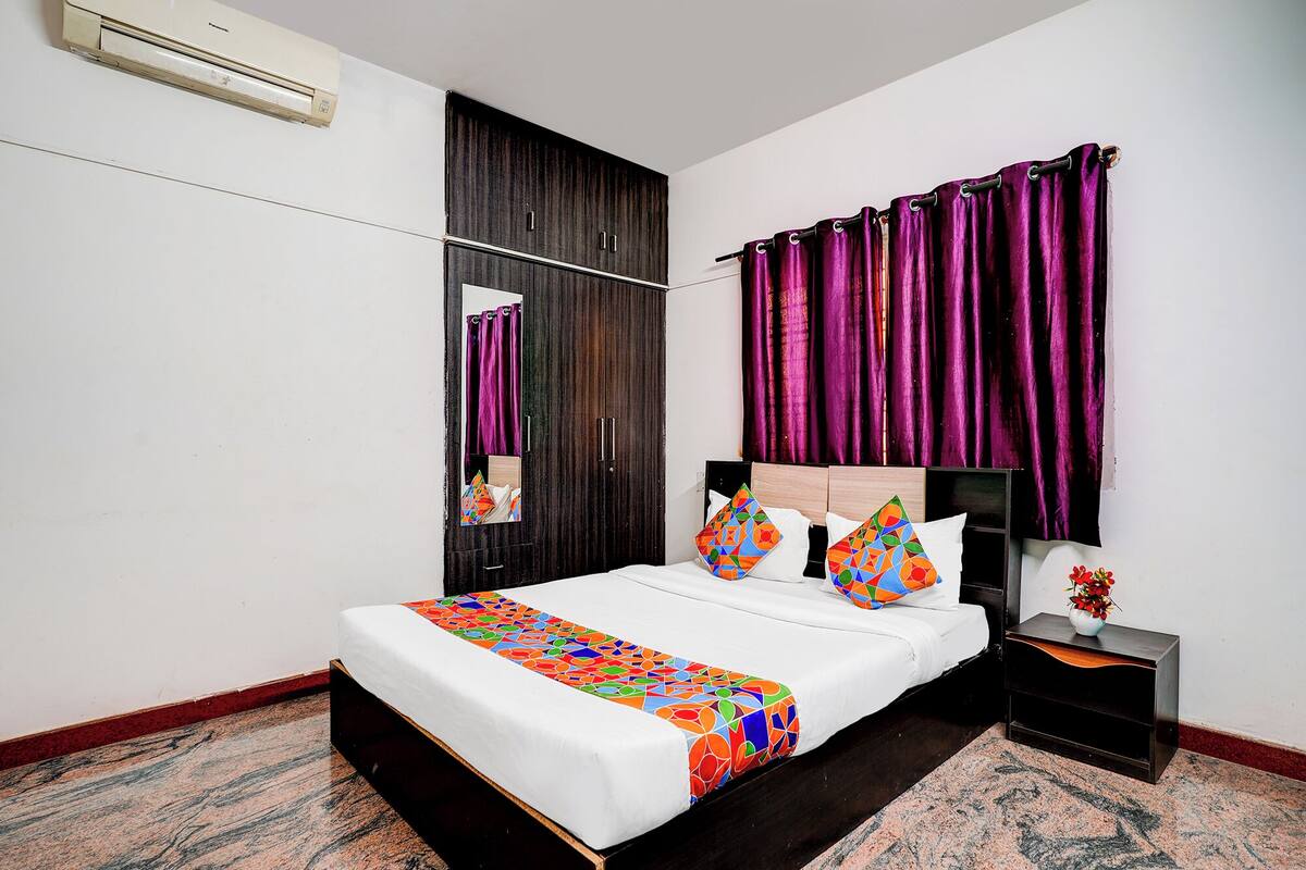 A bedroom with a bed, a nightstand, a mirror, and purple curtains.