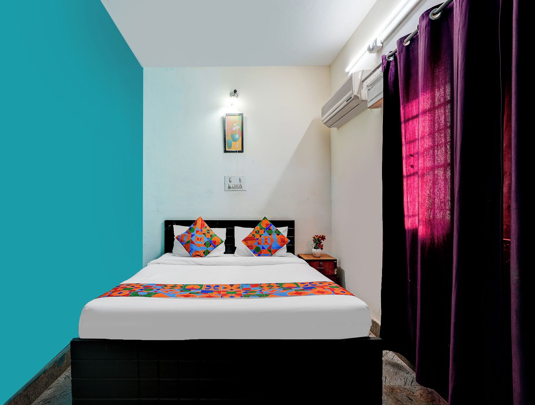 Une chambre à coucher comprenant un lit, une table de chevet, un climatiseur fixé au mur et une fenêtre avec des rideaux.