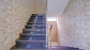 Un escalier avec une rampe en métal, menant à une pièce dont un mur est en briques et qui possède une fenêtre.