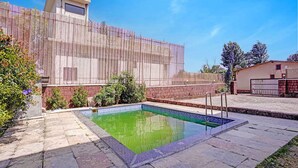 Une piscine avec un bord carrelé, une clôture en bois et un mur en briques.